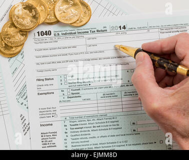 Caucasian hand with pen and solid gold eagle coins on USA tax form 1040 for year 2014 illustrating payment of taxes on forms for Stock Photo