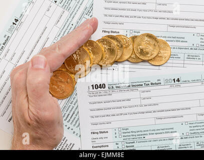 Caucasian hand protecting wealth in solid gold eagle coins on USA tax form 1040 for year 2014 illustrating keeping assets away f Stock Photo