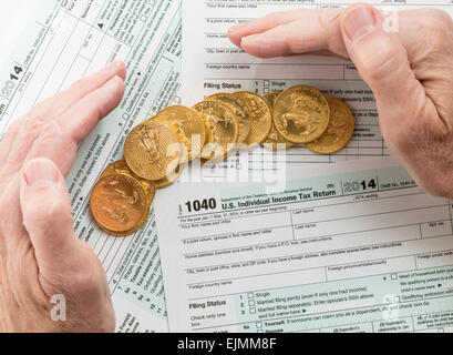 Caucasian hand protecting wealth in solid gold eagle coins on USA tax form 1040 for year 2014 illustrating keeping assets away f Stock Photo