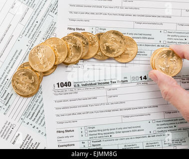 Caucasian hand counting solid gold eagle coins on USA tax form 1040 for year 2014 illustrating payment of taxes to the IRS Stock Photo