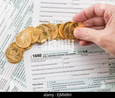 Caucasian hand counting solid gold eagle coins on USA tax form 1040 for year 2014 illustrating payment of taxes to the IRS Stock Photo
