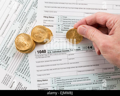 Caucasian hand counting solid gold eagle coins on USA tax form 1040 for year 2014 illustrating payment of taxes to the IRS Stock Photo