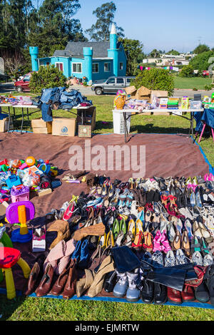 A yard sale in the front lawn of an unusual house shaped like a small castle and painted a turquoise color. Stock Photo
