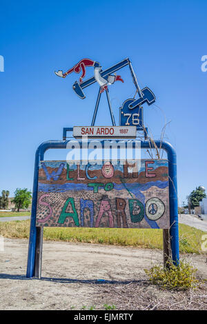 The welcome to San Ardo sign featuring a sculpture of a oil drilling pumpjack with a cowboy with spurs on riding the oil rig. Stock Photo