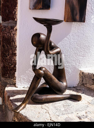 Small abstract bronze female human figure sitting on a step while holding up a bowl. Stock Photo