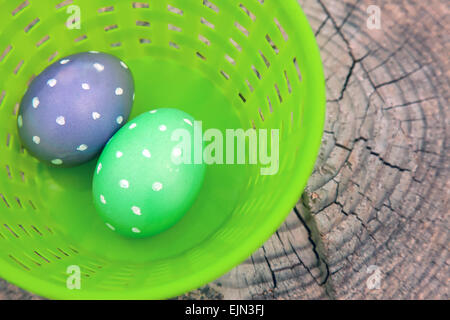 Two dotted Easter eggs in a plastic basket sitting on a wood stump Stock Photo