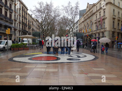 People on rainy day walking along Las Ramblas and Joan Miro mosaic, Barcelona, Catalonia, Spain Stock Photo