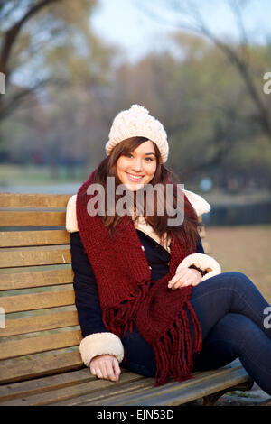 Young girl sitting on bench in a park in the Winter looking at camera Stock Photo