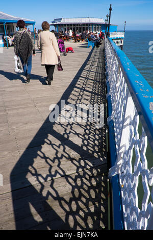 People walking on Llandudno pier in sunshine with shadows from cast iron railings, Conwy, Wales. Stock Photo