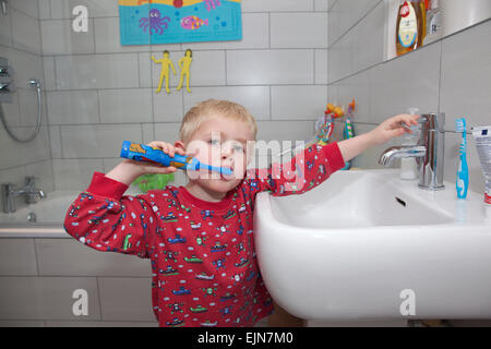 Four year old boy brushing his teeth with an electric toothbrush in the bathroom before bedtime, UK Stock Photo