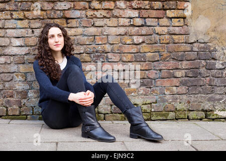 young woman sitting up against a brick wall Stock Photo
