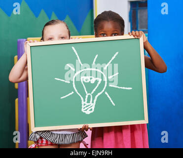 Two children holding a chalkboard with a lightbulb drawn on it Stock Photo