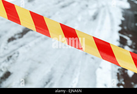 Red and yellow striped tape on winter road. Restricted area border Stock Photo