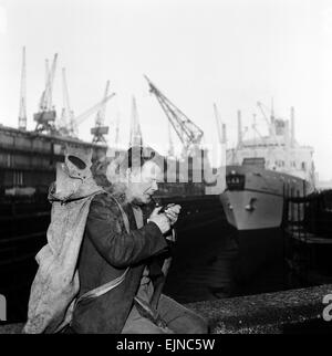 Unemployed and views of Liverpool, Merseyside, 30th November 1962. Carpenter lights his pipe down at the docks. Stock Photo