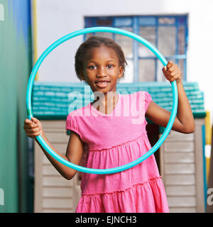 Happy african girl playing with hula hoop in kindergarten Stock Photo