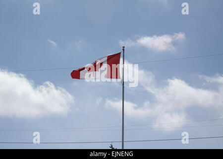 Canadian Flag on a tall flagpole gently waving in a light breeze against clouds and blue sky. Stock Photo