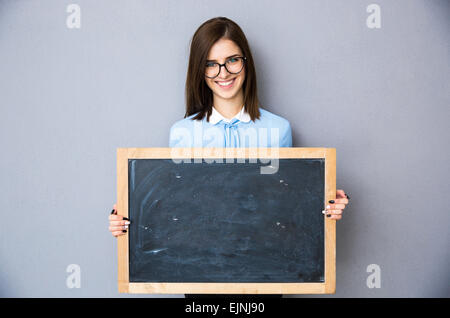 Smiling woman standing with billboard over gray background. Wearing in blue shirt and glasses. Looking at camera Stock Photo