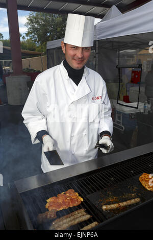 Chef tending a barbecue dressed in white chefs clothes smiling at camera Stock Photo