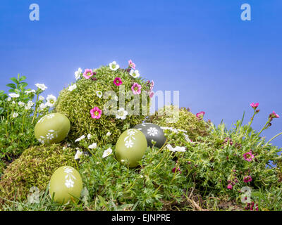 Easter eggs scattered in the grass and giant moss-grown egg with fresh spring flowers over blue sky Stock Photo