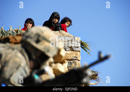 Afghan children on a rooftop watch a U.S. Army Soldier below as he performs perimeter security during a mission in the village of Miricalai, Khowst province, Afghanistan, Nov. 11, 2009. The Soldiers are assigned to the 25th Infantry Division's Company D, 1st Battalion, 501st Regiment, 4th Brigade.  Spc. Christopher Nicholas Stock Photo