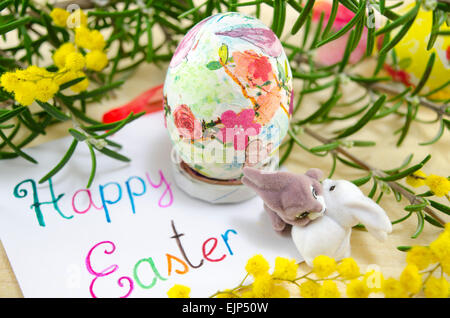 Hand painted decoupage Easter egg on wooden surface with a Happy Easter card and two toy rabbits Stock Photo