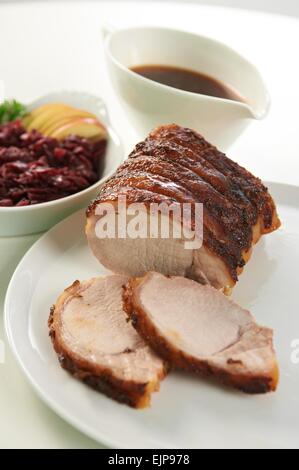 Sunday roast pork lunch gravy boat red cabbage apple slices crackling round white plate Stock Photo