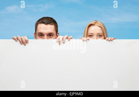 happy couple hiding behind big white blank board Stock Photo