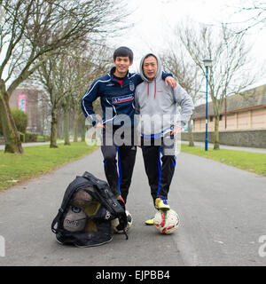 A father and son, ethnic Chinese, together after going football soccer training in a park on a cold grey winter morning UK Stock Photo