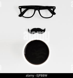 high-angle shot of a white table with a pair of black plastic-rimmed eyeglasses, a fake moustache and a cup of coffee, depicting Stock Photo