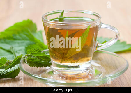 wide shot of medicinal nettle tea with fresh herbs inside teacup, stinging nettle leaves around, wooden floor, Stock Photo