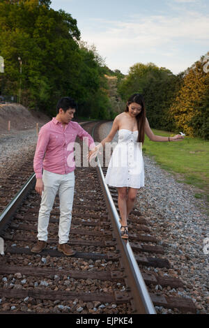 Romantic Asian couple playing outside on railroad tracks, being affectionate and smiling Stock Photo