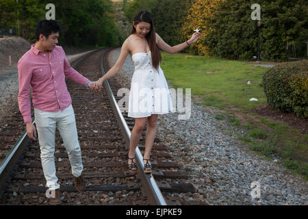 Romantic Asian couple playing outside on railroad tracks, being affectionate and smiling Stock Photo