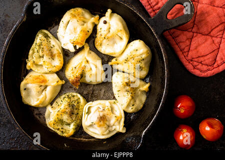Fried Russian pelmeni with meat in a frying pan. Near potholder and tomatoes. top view Stock Photo