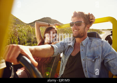 Woman looking at man driving car on a summer day. Loving young couple on road trip. Stock Photo