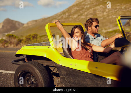 Relaxed couple enjoying in the car ride. Beautiful young woman looking at a view with her boyfriend driving the car on a summer Stock Photo