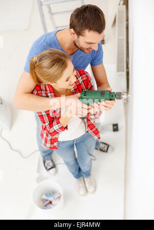 smiling couple drilling hole in wall at home Stock Photo