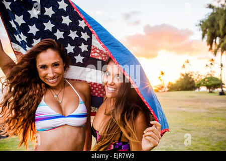 Women standing under American flag quilt at sunset Stock Photo
