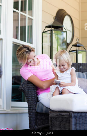 Caucasian mother and daughter using cell phone on porch Stock Photo