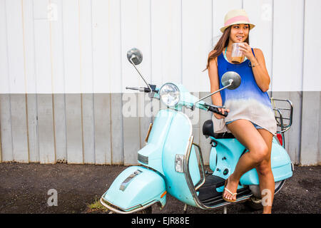 Pacific Islander woman drinking iced coffee on scooter Stock Photo