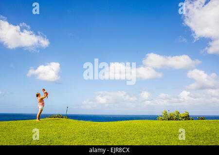 Mother and child playing in grass field under blue sky Stock Photo