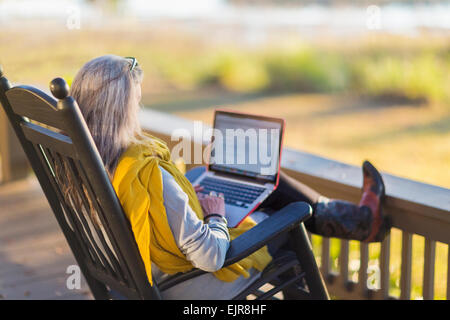 Older Caucasian woman using laptop on porch Stock Photo