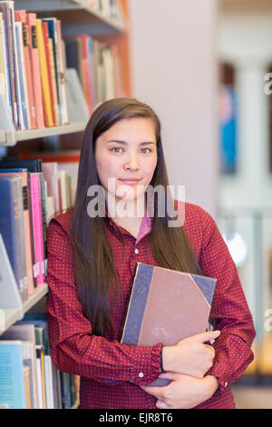 Mixed race student holding book in library Stock Photo