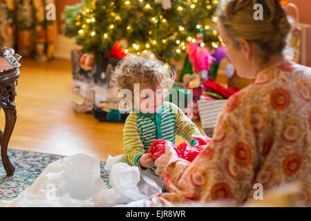 Caucasian mother and baby son opening presents near Christmas tree