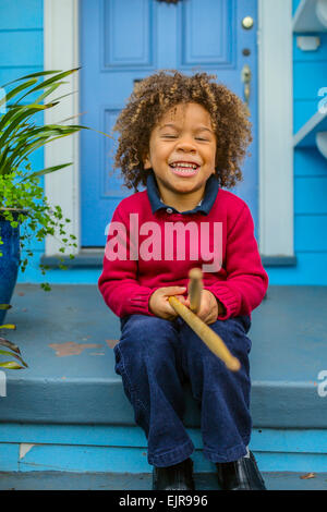 Pacific Islander boy with drumsticks sitting on front stoop Stock Photo