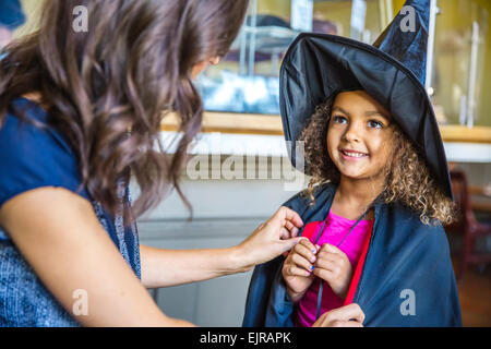 Mother dressing daughter in witch costume Stock Photo
