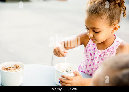 Mixed race girl eating ice cream at outdoor cafe