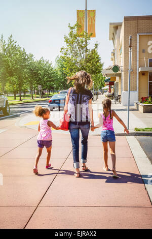 Mother and daughters holding hands on neighborhood sidewalk Stock Photo