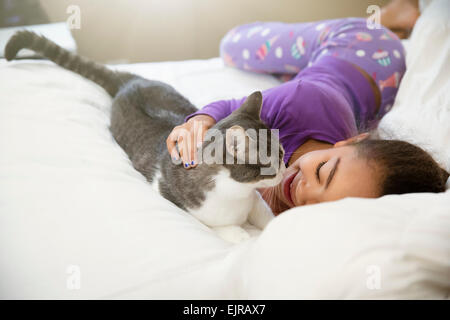 Mixed race girl playing with cat on bed Stock Photo