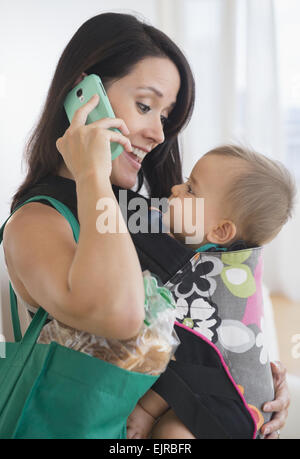 Mixed race mother carrying baby and talking on cell phone Stock Photo