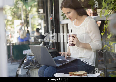 Caucasian woman using laptop and drinking coffee outside cafe Stock Photo